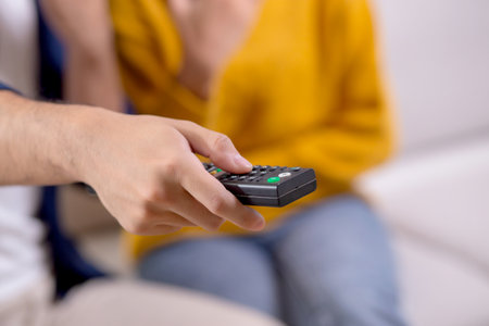 Closeup hands of couple sitting on cozy sofa watching TV and pushing remote control a relaxation in living room at home, relationship and comfortable of couple during watching television on couch.の写真素材