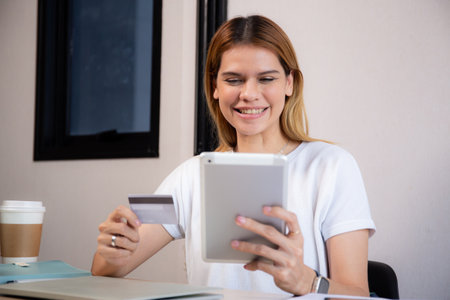 Happy young caucasian woman holding credit card or debit card paying with shopping online while looking tablet with satisfied, woman with spending with transaction of finance, business and financial.の写真素材
