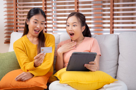 Two young asian woman sitting on sofa using tablet computer shopping online with credit card buying to internet, female payment with business, purchase and payment, business and finance.の写真素材
