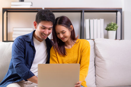 Young asian couple looking on laptop for relax with cozy and contentment sitting on sofa in living room at home, couple leisure watching laptop on couch, relationship and bonding, lifestyle concept.の写真素材