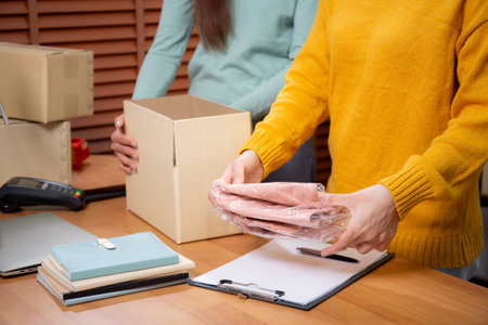 Closeup hand of woman packing in cardboard box for shipping or storage in home office, online seller packing clothes in box for delivery, logistic and cargo, service of retail.の写真素材