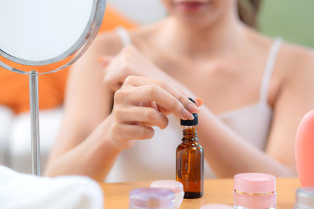 Closeup hands beautiful young woman applying lotion herb on hands looking mirror at home, beauty woman dropper serum for rejuvenation on hands, cosmetic and makeup for self care, skin care and health.の写真素材