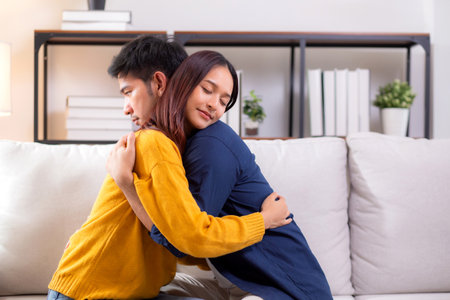 Young asian couple hug sitting on sofa with affectionate in living room at home, husband and wife with gentle and relation with cozy and love while embrace, bonding and comfort, couple and lifestyle.の写真素材