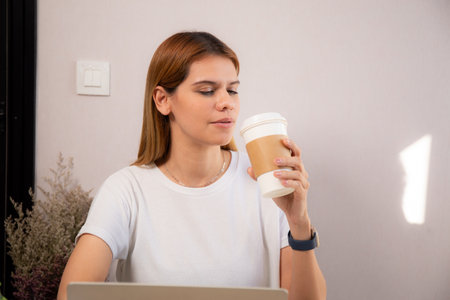 Happiness young caucasian businesswoman drinking coffee while working on laptop computer in home office, happy business woman drinking beverage while using laptop for relax, business concept.の写真素材
