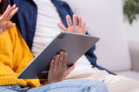 Closeup happy asian couple video call on tablet sitting on sofa in living room at home, hand waving...