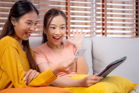 Two young asian woman sitting on sofa using tablet computer shopping online with credit card buying to internet, female payment with business, purchase and payment, business and finance.の写真素材