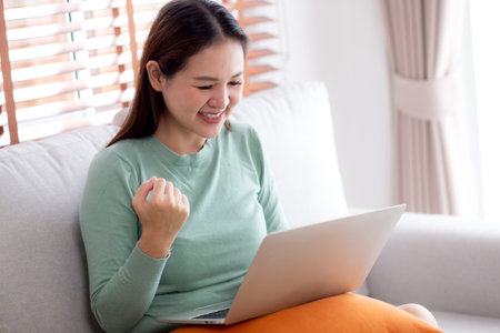 Young asian business woman working with laptop sitting on sofa in home office, businesswoman using on notebook in living room at home, woman relax with using laptop while success, business concept.の写真素材