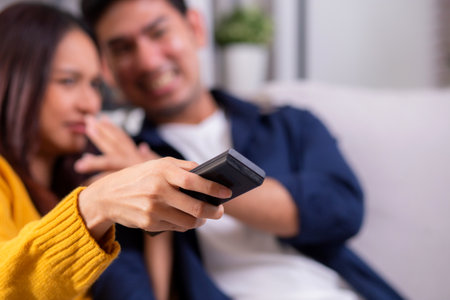 Closeup young asian couple watching a scary or thrilling TV show in living room with emotion shock and scared, emotion reaction while watching horror television with fear, lifestyle and bonding.の写真素材