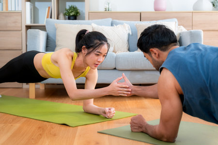 Young asian couple practicing workout with plank while high-five in living room at home, man and woman training exercise for challenge together, motivation and strength of muscle for health.の写真素材