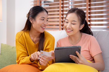 Two young asian woman sitting on sofa using tablet computer shopping online with credit card buying to internet, female payment with business, purchase and payment, business and finance.の写真素材