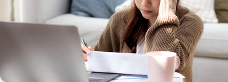 Young asian woman checking document about finance with stress and worried in living room at home, woman looking bill financial about debt and expenses with anxiety, business and finance.の写真素材