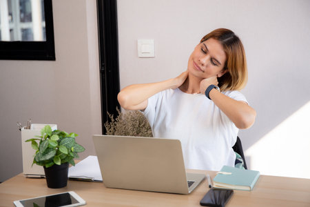 Young caucasian businesswoman working on laptop while stretch muscle neck in home office, business woman overworked on notebook while exhausted in office, business and medical.の写真素材