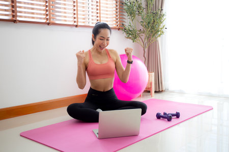 Young asian woman watch laptop for practice yoga and workout in living room at home, woman using chat bot on notebook with artificial intelligence with for training and exercise, sport and wellbeing.の写真素材