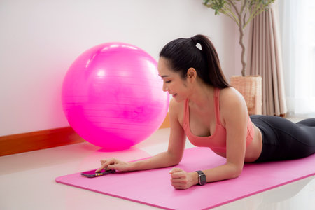 Young asian woman practicing workout and posing plank on mat while motivated and determined at home, female doing weight training with strength and strong, one person, lifestyles and sport concept.の写真素材