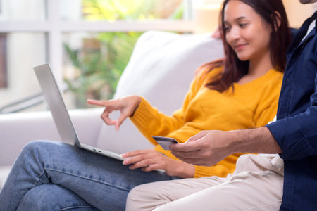 Closeup happy asian couple using laptop and credit card for online shopping together in living room at home, man and woman relax with enjoy a digital lifestyle, convenient payment.の写真素材