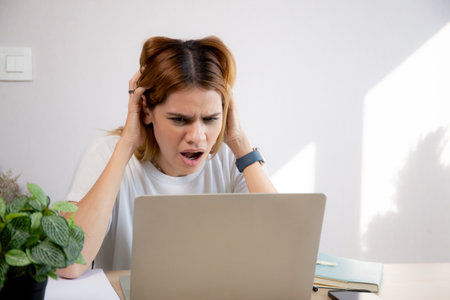 Unhappy young caucasian businesswoman using laptop computer on desk with stress and burnout at home office, business woman working on laptop with frustrated and anxiety, business and expression.の写真素材