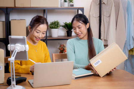 Two young asian woman working while planning online business and checking order with writing on tablet at home, retail with online seller, startup business and cargo, shipping and service.の写真素材