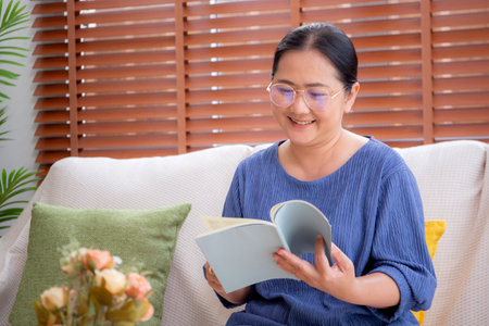 Asian senior woman reading a book sitting on sofa with relax in living room at home, elderly woman reading literature on couch with cozy, hobby and recreation in weekend, lifestyles concept.の写真素材
