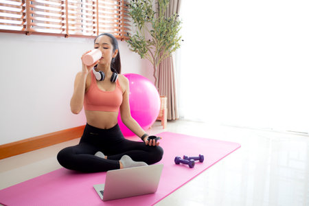 Young asian woman in sportswear drinking water in bottle after workout and exercise in living room at home, woman relax drinking beverage for health after workout, sport and motivation for health.の写真素材