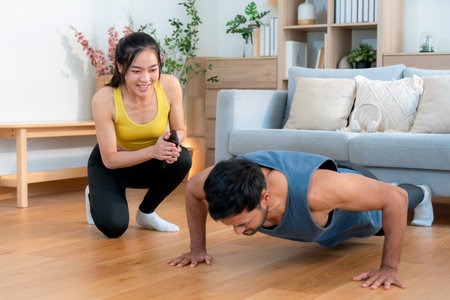Young asian couple workout during woman hold smartphone encouragement to partner while man doing pushup with motivation, woman cheering man with exercise with strong and strength, self-care.の写真素材