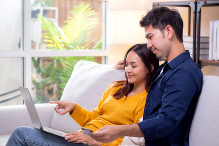 Happy asian couple using laptop and credit card for online shopping together in living room at home, man and woman smiling and relax with enjoy a digital lifestyle, convenient payment.の写真素材