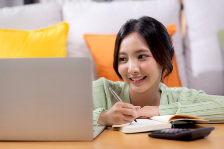Young asian woman planning and strategy about finance and investment or tax while writing on textbook in living room at home, woman with expense and budget of home, business and finance.の写真素材
