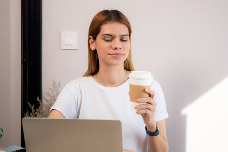 Happiness young caucasian businesswoman drinking coffee while working on laptop computer in home office, happy business woman drinking beverage while using laptop for relax, business concept.の写真素材