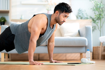 Young asian man doing pushup exercise in living room at home with determination, man training on yoga mat, bodybuilding strength and fitness for healthy lifestyle, workout routine, self-care.の写真素材