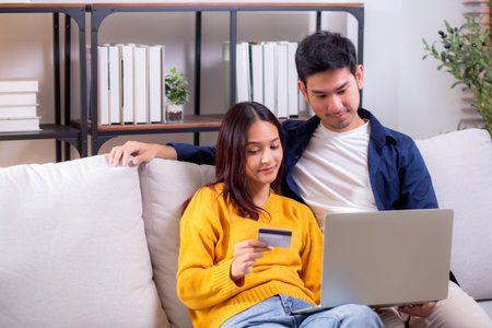 Happy asian couple using laptop and credit card for online shopping together in living room at home, man and woman smiling and relax with enjoy a digital lifestyle, convenient payment.の写真素材