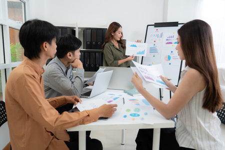 Group asian business team meeting in office about report marketing and finance with presenting charts and graph while colleagues discuss report and strategy, teamwork planning and analysis.の写真素材