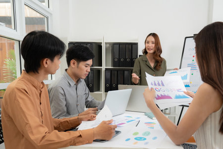 Group asian business team meeting in office about report marketing and finance with presenting charts and graph while colleagues discuss report and strategy, teamwork planning and analysis.の写真素材
