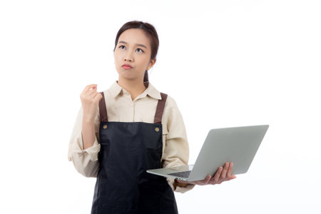 Portrait young asian business woman wearing apron holding laptop computer isolated white background, waitress or barista holding laptop computer while thoughtful, cut out, business or freelance.の写真素材