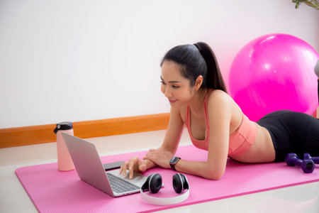 Young asian woman video call with friends after practice yoga and workout for relax in living room at home, woman using notebook for conference after training and exercise, sport and wellbeing.の写真素材