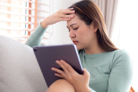 Young asian business woman using tablet computer stress and worried sitting on sofa in living room at home office, businesswoman working on tablet while concerned and tire, business and lifestyle.の写真素材