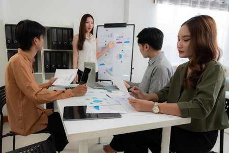 Group asian business team meeting in office about report marketing and finance with presenting charts and graph while colleagues discuss report and strategy, teamwork planning and analysis.の写真素材
