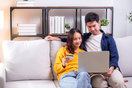 Happy asian couple using laptop and credit card for online shopping together in living room at home, man and woman smiling and relax with enjoy a digital lifestyle, convenient payment.の写真素材