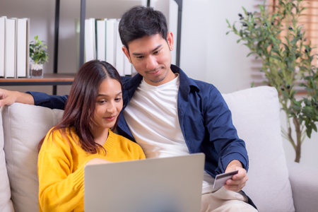 Happy asian couple using laptop and credit card for online shopping together in living room at home, man and woman smiling and relax with enjoy a digital lifestyle, convenient payment.の写真素材