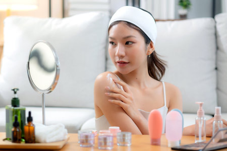 Beauty young asian woman applying cream or lotion while looking mirror in living room at home, happy beautiful woman applying skincare for rejuvenation on shoulder, skin care and health, self care.の写真素材
