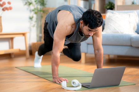 Young asian man doing home workout while watching online tutorial on laptop computer in living room at home, determined and motivation for health, healthy lifestyle and body strength for exercise.の写真素材