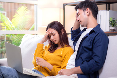 Asian couple looking laptop stressed while financial problem in living room at home, woman using laptop and man hold credit card with upset, couple with expression budget concern and expense.の写真素材