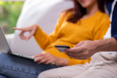 Closeup happy asian couple using laptop and credit card for online shopping together in living room at home, man and woman relax with enjoy a digital lifestyle, convenient payment.の写真素材