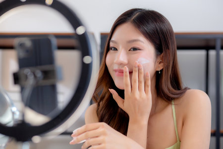 Young asian woman presenting and review cosmetic product with excitement on social media platform for followers, woman review cream or lotion with live streaming, influencer and review cosmetic.の写真素材