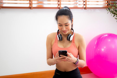 Young asian woman watching smartphone for practice yoga and workout in living room at home, woman using chat bot on smart phone with artificial intelligence with for exercise, sport and wellbeing.の写真素材