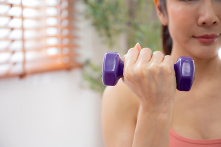 Closeup hand young woman in sportswear workout with dumbbells for strength in living room at home, woman training exercise with determination and challenge with lifting, sport for health.の写真素材