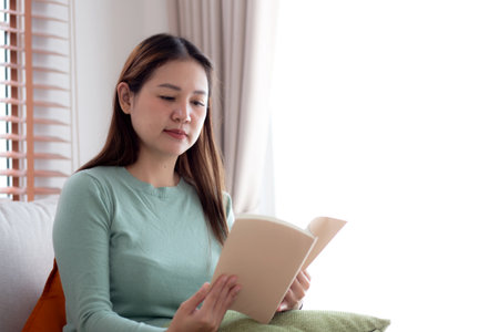 Young asian woman reading a book with expression sitting on sofa in living room at home, woman relax and leisure sitting on couch reading literature, activity and hobby, lifestyle and relaxation.の写真素材