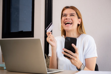 Happy young caucasian woman holding credit card or debit card paying with shopping online while laughing on smartphone, woman with spending with transaction of finance, business and financial.の写真素材