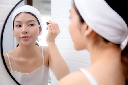 Beautiful young asian woman applying serum for rejuvenation on facial looking mirror, beauty woman applying collagen for treatment skin, self-care, skincare and makeup, cosmetic and makeup.の写真素材