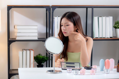 Young asian woman looking face with mirror for checking skin problem with worry expression at home, skincare and beauty concern, dermatology and wellness, woman examining facial skin with stress.の写真素材