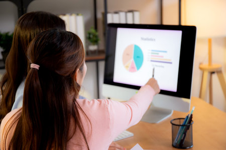 Two asian businesswoman collaborating on data analysis marketing financial with charts at home office, working together with graphs on computer screen, teamwork and marketing strategy planning.の写真素材
