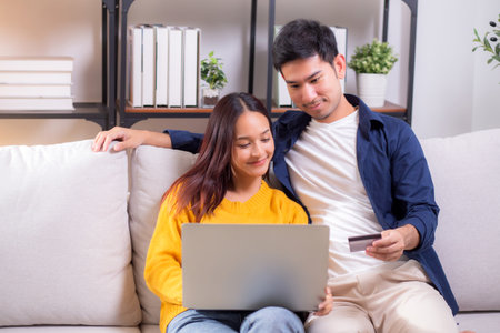 Happy asian couple using laptop and credit card for online shopping together in living room at home, man and woman smiling and relax with enjoy a digital lifestyle, convenient payment.の写真素材